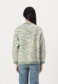 Maglione leggero in maglia di colore verde menta e crema, caratterizzato da un morbido motivo a zebra testurizzato. Collo tondo classico e spalle ribassate.