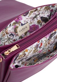 Bolso de piel morado abierto para mostrar un forro de tela floral con mariposas y un bolsillo con cremallera dorada, que presenta una etiqueta de marca beige.