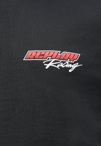 Μαύρο βαμβακερό μπλουζάκι με γραφικό "REPLAY Racing" σε κόκκινο και λευκό χρώμα, με έντονα γράμματα και καλλιγραφικό στυλ. Μαλακή υφή.
