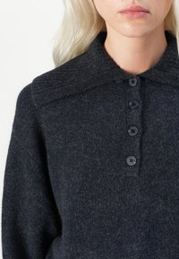Sweter z dzianiny w ciemnoszarym kolorze o miękkiej fakturze, z dużym kołnierzem, zapinany na guziki z przodu, z czterema czarnymi guzikami.