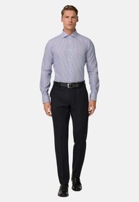 Svetlo modra prugasta srajca z ožjim krojem, dolgimi rokavi in s kravato s gumbi, v kombinaciji z temnimi hlačami in črnimi formalnimi čevlji.