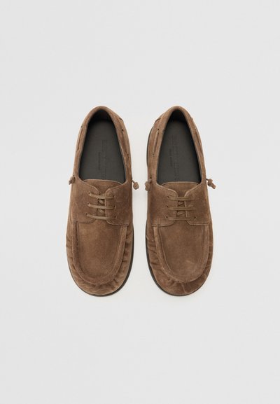 Brown suede shoes with a rounded toe, lace accents, and a cushioned sole, featuring a smooth texture and minimalistic design.