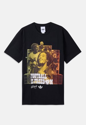 Camiseta negra con gráfico multicolor de Bob Marley y escenas de fútbol, texto "El fútbol es libertad", logos de Adidas y firma abajo.