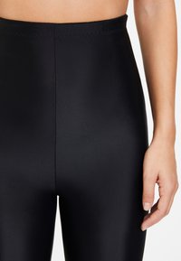 Högmidjade svarta tights tillverkade av ett glatt, stretchigt material. Har en ren finish och subtil sömnad längs midjebandet.