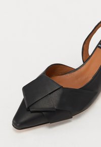 Chaussure slingback en cuir noir avec un bout pointu ; présente un grand nœud texturé à l'avant et un intérieur lisse beige.