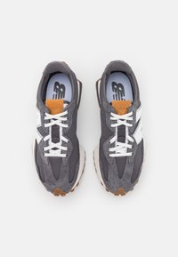 Grå idrottsskor tillverkade av mocka och tyg, med vita accenter, brun sula och vita skosnören. Utmärkande vadderad tunga och strukturerad design.