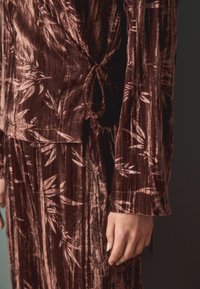 Braunes Samtoberteil mit einem Bambusblattmuster, langen Ärmeln und einer gebundenen Taillendetail. Weicher Textur mit einem glatten, fließenden Design.