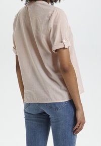 Camicetta a righe rosa chiaro con maniche corte e risvolti, colletto e vestibilità rilassata, abbinata a jeans blu slim-fit.
