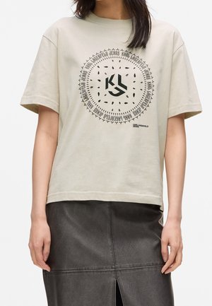Beige lyhythihainen t-paita, jossa musta pyöreä Karl Lagerfeld Jeans -logo, yhdistetty mustaan nahkahameeseen, jossa on etuviilto.