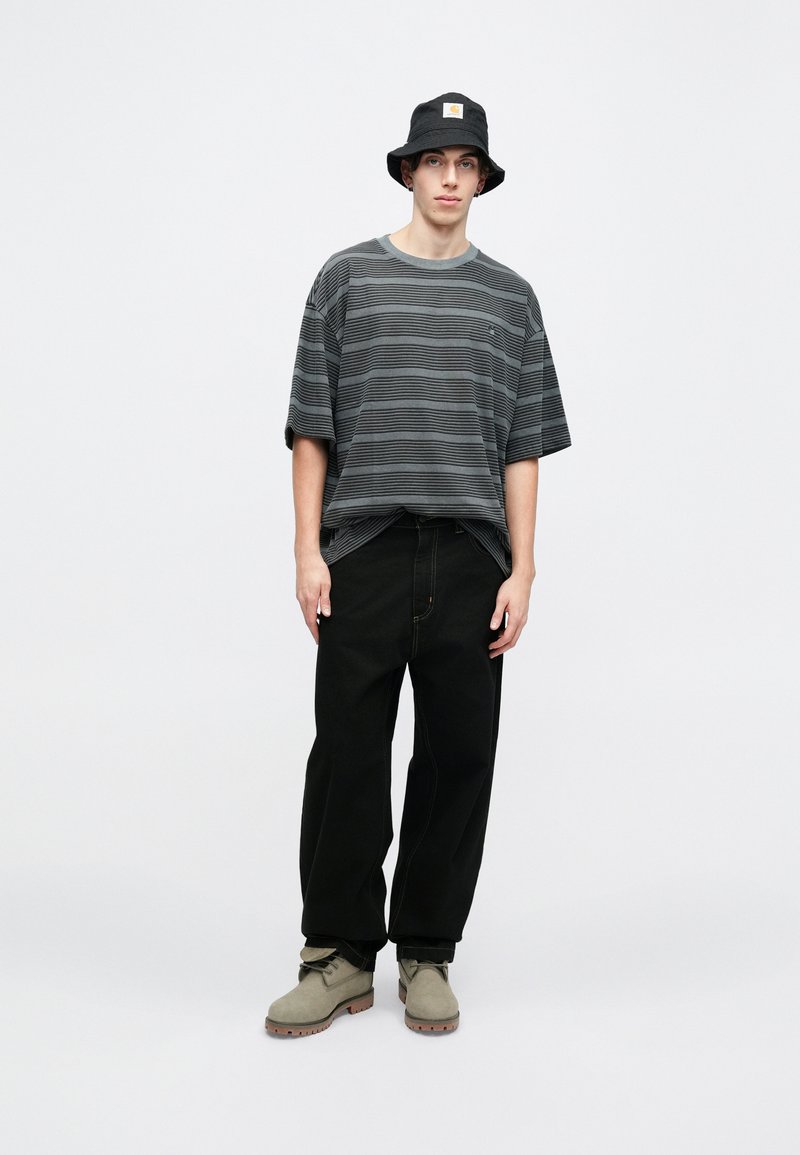 Gray striped short-sleeve t-shirt, black wide-leg pants, olive green boots, and a black bucket hat with a patch logo.