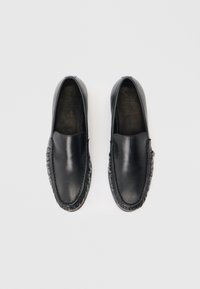 Ζευγάρι μαύρα δερμάτινα μοκασίνια χωρίς κορδόνια με στρογγυλεμένες μύτες και διακοσμητικές ραφές, ορατά από πάνω σε λευκό φόντο.