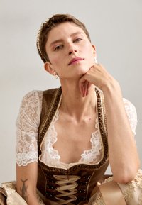 Tenue traditionnelle avec un corsage brun agrémenté de dentelle, de courtes manches en dentelle et une jupe détaillée. Coiffure de trône dorée et boucles d'oreilles.