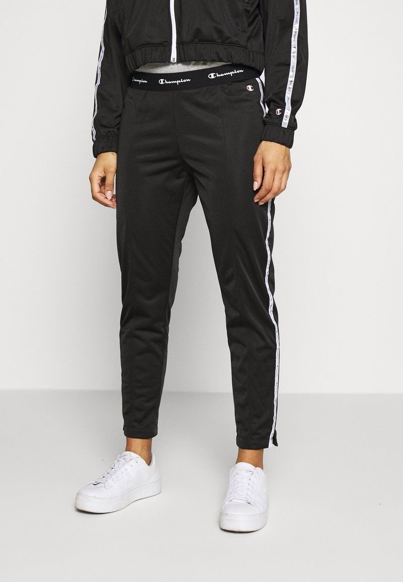 Svarta sportbyxor i slät tyg med figursydd design, försedd med vita sidostreck och resårmidja med logotyp.