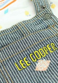 Bretelles en denim avec un motif rayé, broderie jaune "LEE COOPER", matériel en métal pour les boutons et détails de couture contrastants.
