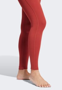 Czerwone legginsy sportowe wykonane z elastycznego materiału, charakteryzujące się dopasowanym krojem z kontrastowymi szwami i długością do kostek.
