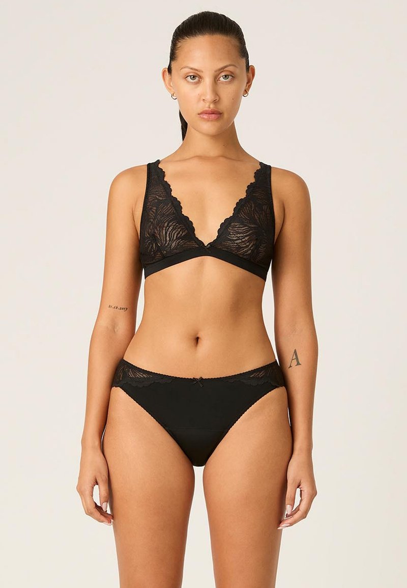 Bralette en dentelle noire avec un décolleté plongeant et des bords festonnés, assortie à une culotte noire ornée de dentelle.