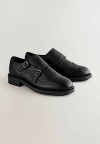 Mustat nahkakengät pyöreällä varvalla, koristeellisella brogue-yksityiskohdalla, soljetta ja paksua kumipohjaa.
