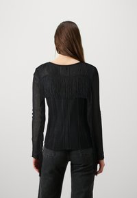 Svart långärmad topp med ribbad textur. Har fransdetaljer längs axlarna och en rund halsringning. Matchas med mörka byxor.