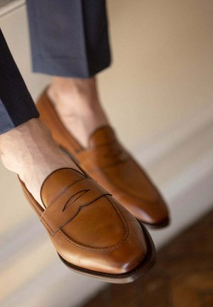 Bruine leren loafers met een puntige neus, voorzien van een gestikt bandje over de bovenkant en een gladde, gepolijste afwerking. Minimalistisch ontwerp.