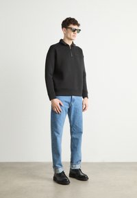 Hanorac negru cu fermoar, blugi drepti de culoare albastru deschis, pantofi negri. Modelul poartă ochelari de soare închiși la culoare; design simplu, tivuri de pantaloni manșonate.