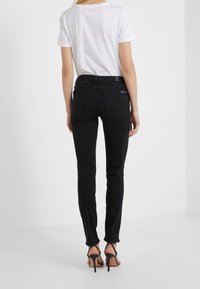 Vaqueros negros ajustados con cintura media, hechos de tela de mezclilla, con bolsillos traseros y una textura suave. Combinados con una camiseta blanca básica.