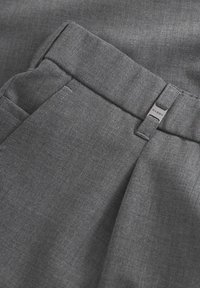 Hallhalli kangast püksid, millel on sile tekstuur, kohandatud disain ja nähtav metallist silt logo detailiga vöökoha lähedal.