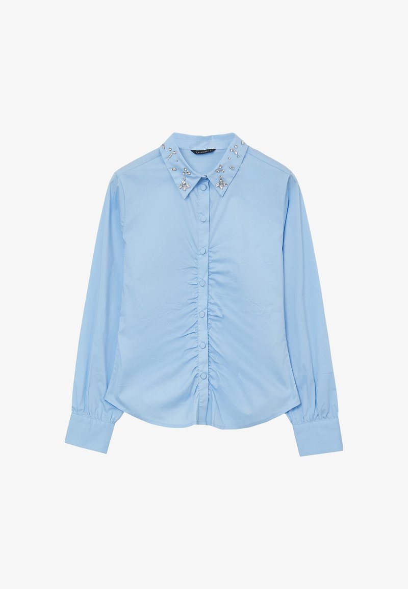 Blouse bleu clair à manches longues avec boutons froncés sur le devant et col orné de perles et de pierres argentées.