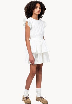 Vestito bianco con motivo a occhiello, maniche arricciate, gonna a balze e vita elasticizzata, abbinato a scarpe beige e calzini bianchi.