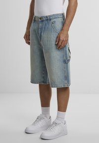 Lichtblauwe denim shorts met een ontspannen pasvorm, riemlussen en zijzakken. Gecombineerd met witte sneakers en enkellange sokken.