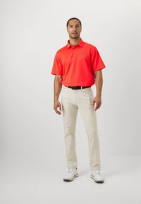 Röd pikétröja med korta ärmar och treknappslinning, kombinerad med ljusbeige byxor och vita golfsparkar. Enkel, ren design.