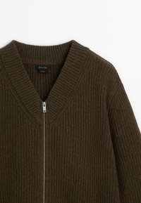 Cardigan en laine marron côtelé avec col en V et fermeture éclair argentée à l'avant, montrant le haut du torse et la zone du col.