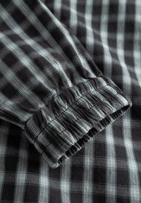 Poignet à manches longues avec bande élastique sur tissu à carreaux noir et gris montrant des détails froncés et un motif en grille.