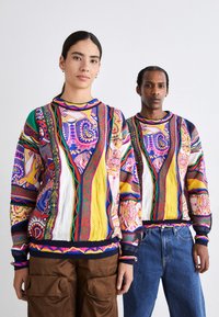 Kolorowy, wzorzysty sweter z mieszanką geometrycznych wzorów w odcieniach różu, żółci, zieleni i niebieskiego; zawiera ściągacz przy mankietach i u dołu.