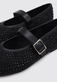 Black Mary Jane shoes with rhinestone embellishments. Features a rounded toe, leather strap with a silver buckle, and textured surface.