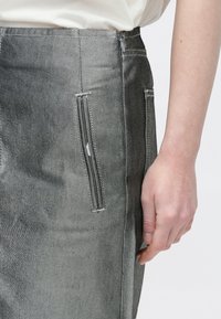 Szürke, strukturált anyagból készült farmer szoknya finom halszálka mintával, oldalzsebekkel és hátul cipzárral.