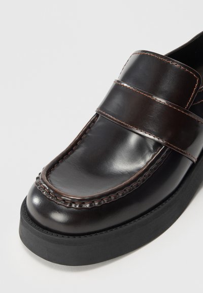Brown leather loafer with double strap detail, contrasting stitching, rounded toe, and rubber sole. Smooth texture and polished finish.