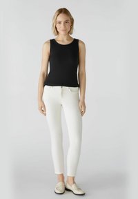 Zwarte geribbelde tanktop, witte nauwsluitende jeans en lichtbeige instapschoenen. Eenvoudig ontwerp zonder patronen, met een gladde textuur en slim fit.