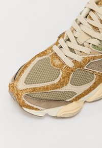 Gros plan sur la pointe d'une basket beige et marron avec tissu en mesh, daim, superpositions en daim texturé et lacets épais beiges.