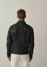 Schwarze Lederjacke mit Kragen, geradem Schnitt und langen Ärmeln. Mit sichtbaren Nähten und einer glatten Textur.
