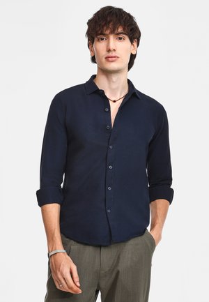 Navyblauwe button-up shirt van gladde stof, met een kraag, lange mouwen opgerold bij de manchetten en een knoopsluiting aan de voorkant.