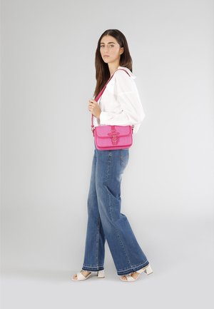 Lyserød crossbody taske med et struktureret stof, flaplukning og dekorativ hardware. Accentueret med en bøjet rem. Båret med lyse denimbukser.