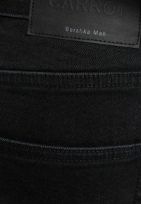 Svarta denimbyxor med en texturerad yta, med sömmar på bakfickorna och en läderetikett med texten "CARROT Bershka Man."