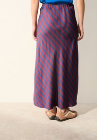 Gonna lunga con righe orizzontali rosse e blu, tessuto leggero, vita elasticizzata e texture morbida, abbinata a calzature marroni.