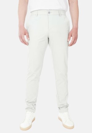 Pantaloni grigi chiari con vestibilità slim, realizzati in un tessuto liscio, con chiusura a bottoni e tasche laterali. Indossati con sneakers bianche.