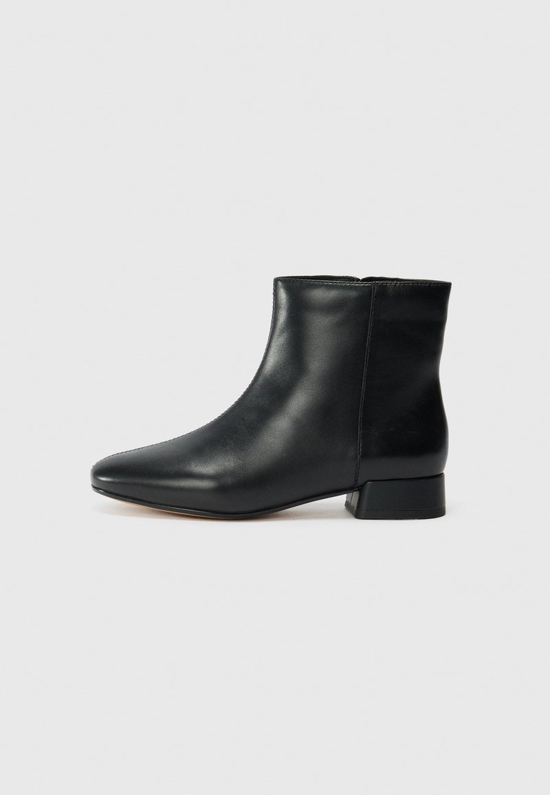 Bottine noire en cuir avec un bout pointu et un petit talon carré, vue de profil sur un fond gris clair.