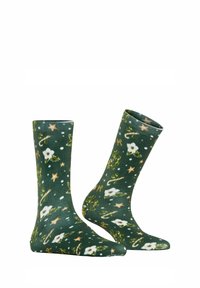 Calzini verdi con un motivo ripetuto di fiori bianchi, stelle, bastoncini di zucchero e nastri su uno sfondo testurizzato.