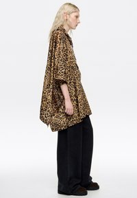 Camisa extragrande de estampado de leopardo en tela sedosa, con un ajuste relajado y mangas cortas, combinada con pantalones negros de pierna ancha y zapatos oscuros.