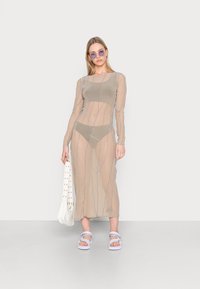Vestido transparente de mangas longas na cor bege claro, com riscas verticais azuis. Combinado com um biquíni a condizer, uma bolsa branca e sandálias cor lavanda.