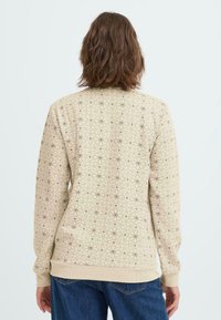 Sudadera beige con un patrón geométrico de pequeñas estrellas marrones, puños y dobladillo acanalados, y un ajuste holgado. Tejido suave, se muestra la vista posterior.