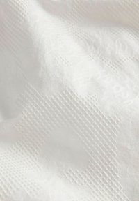 Λευκό ύφασμα με διακριτικά ανάγλυφα γεωμετρικά και λουλουδάτα μοτίβα που δημιουργούν υφασμάτινο σχέδιο σε όλη την επιφάνεια.